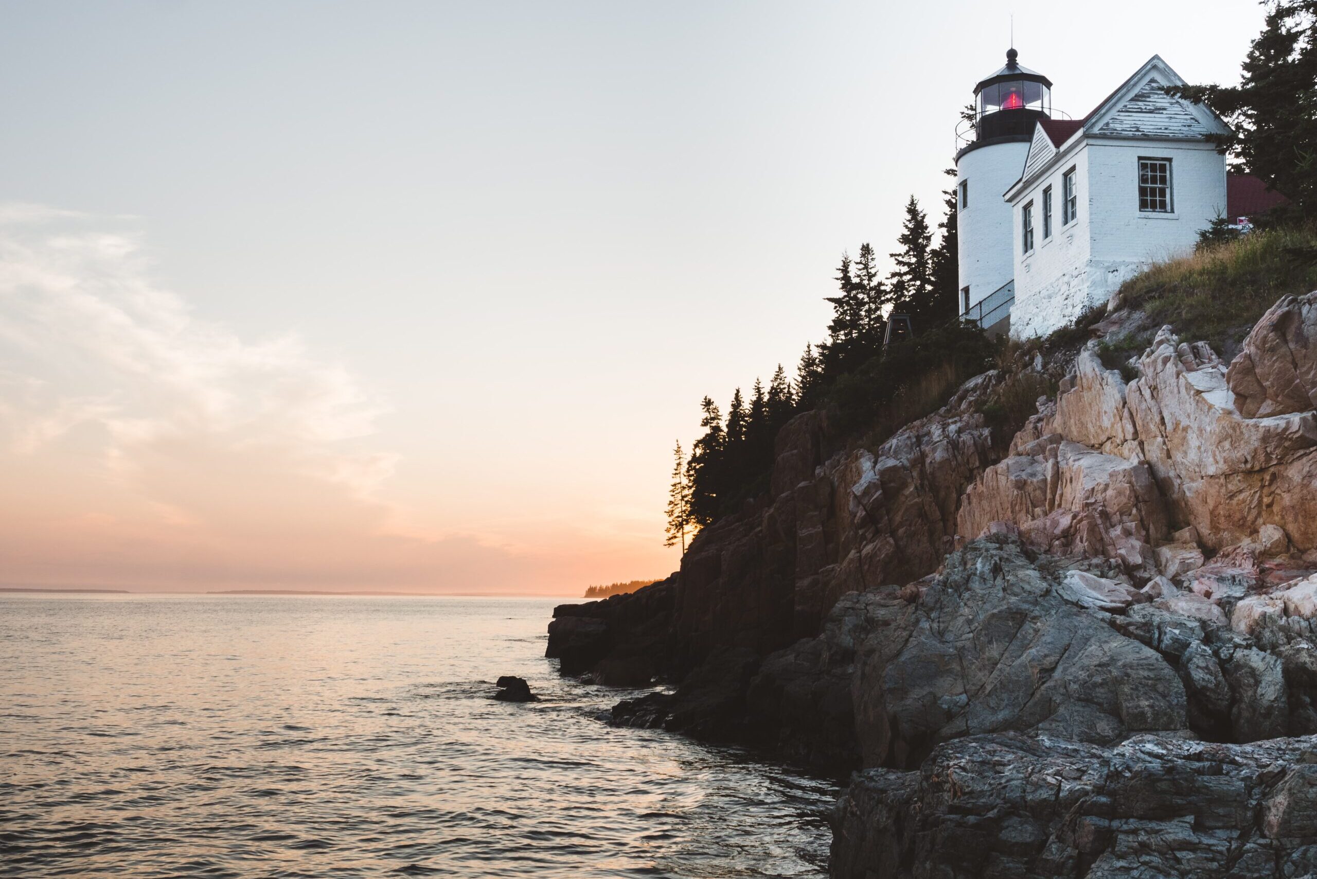 Lighthouse surrounded by pine trees, sits along a rocky cliff on the coast